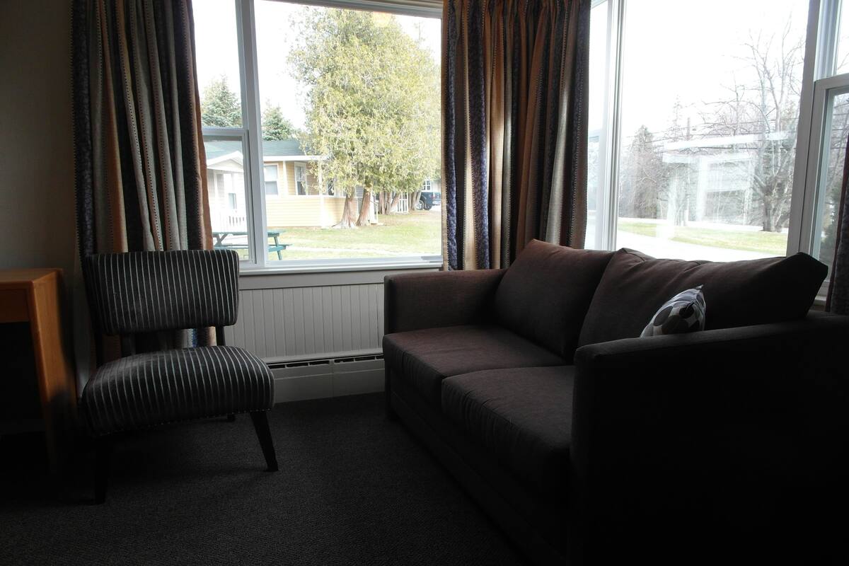 A room with a sofa, a striped chair, and a window with curtains.