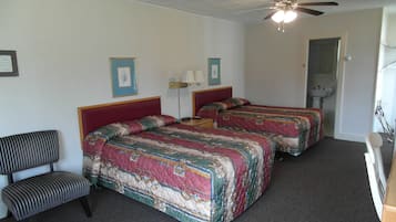 Quarto de hotel com duas camas, uma cadeira, um ventilador de teto e uma pia.