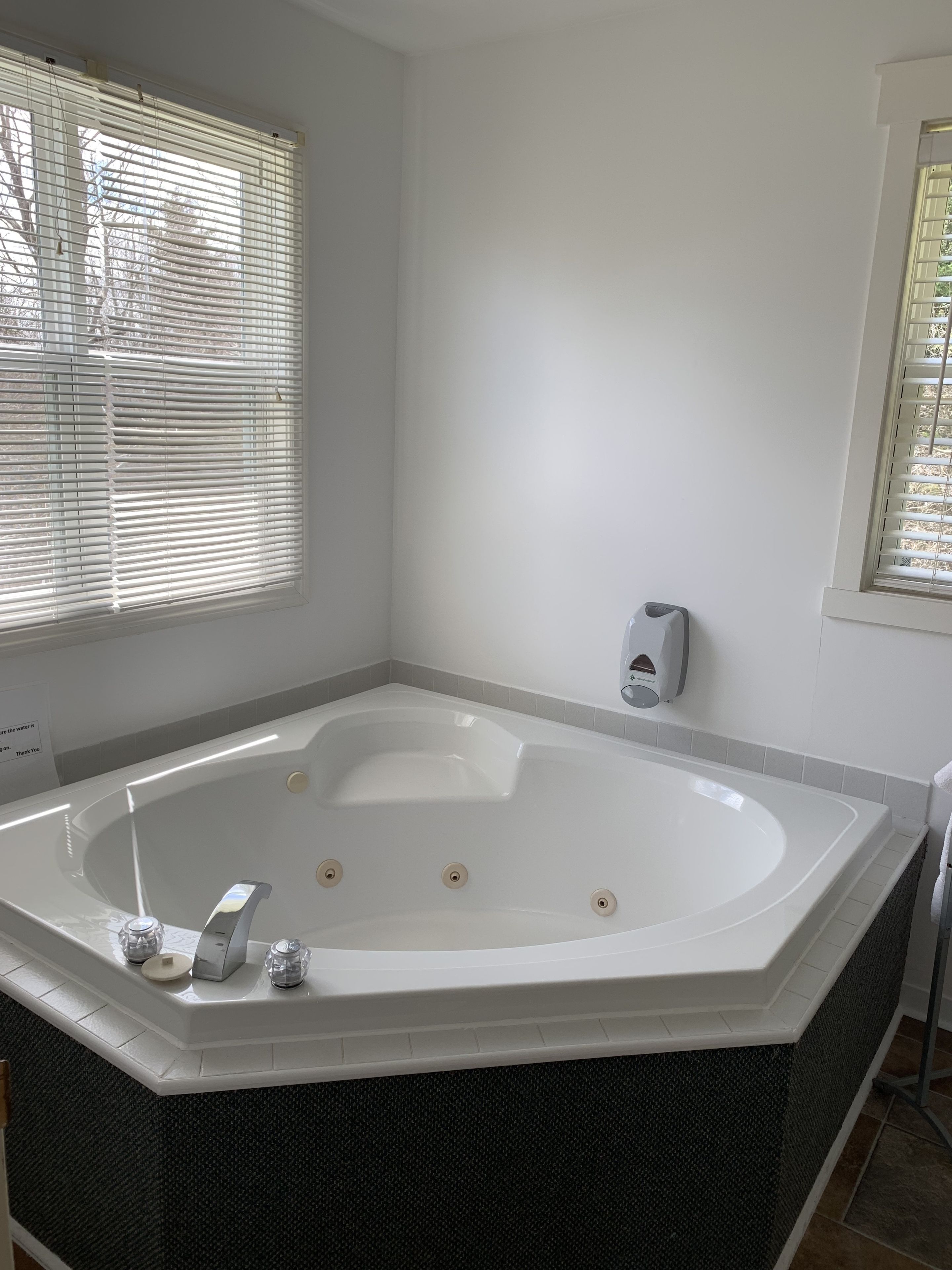 Ein modernes Badezimmer mit einer großzügigen, frei stehenden Badewanne, einem Handseifen-Spender und einem Fenster mit Jalousien.