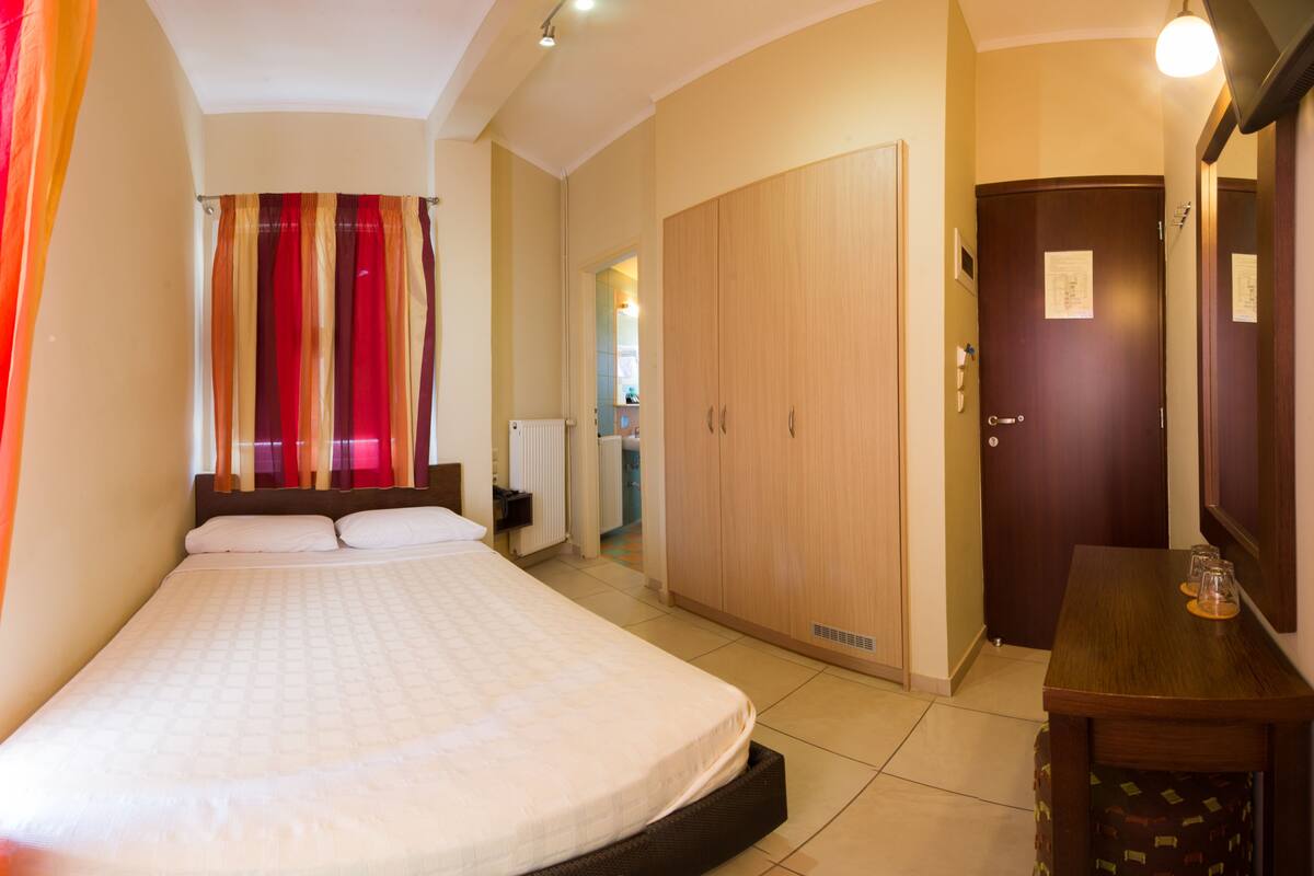 A hotel room with a bed, a wardrobe, a desk, and a bathroom visible through an open door.