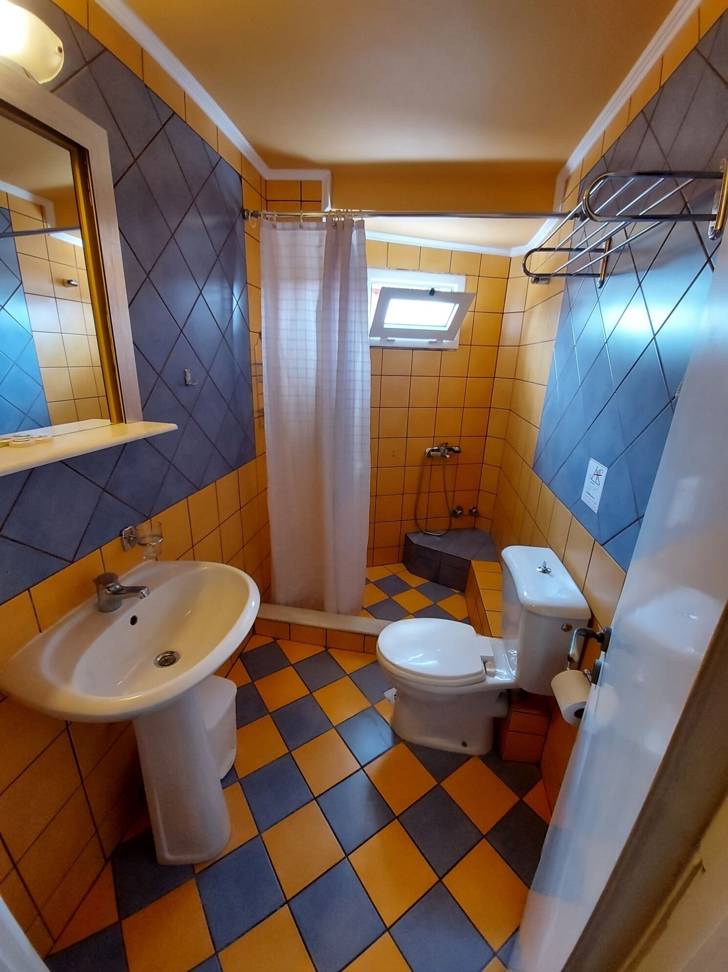 A bathroom with a sink, toilet, and shower area, featuring a checkered floor pattern and a window above the shower.