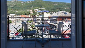 Varanda com duas cadeiras e uma mesa, com vista para uma rua com carros estacionados e edifícios, incluindo uma placa de hotel.