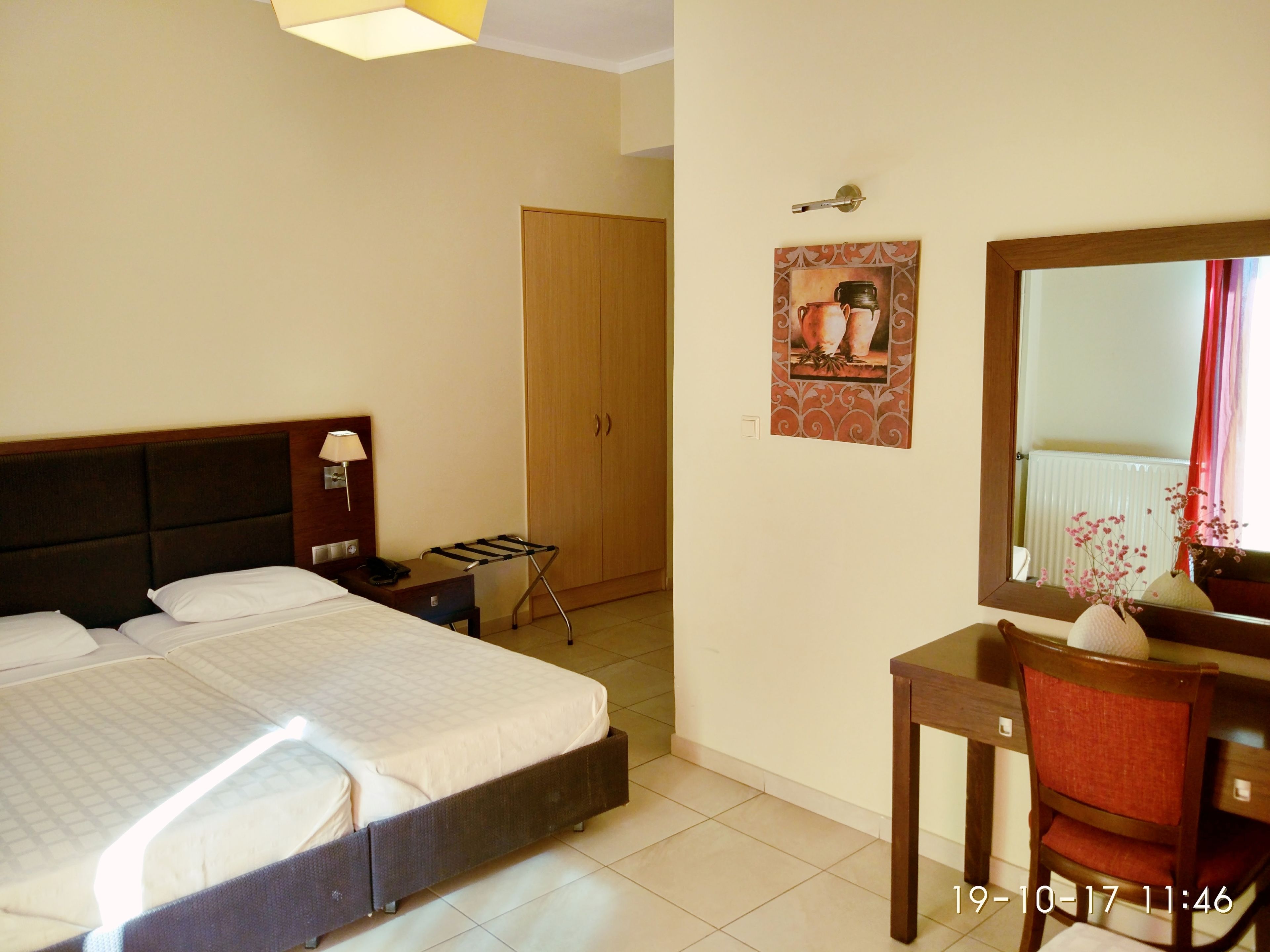 Habitación de hotel con cama, mesita de noche, lámpara, escritorio, silla y espejo.