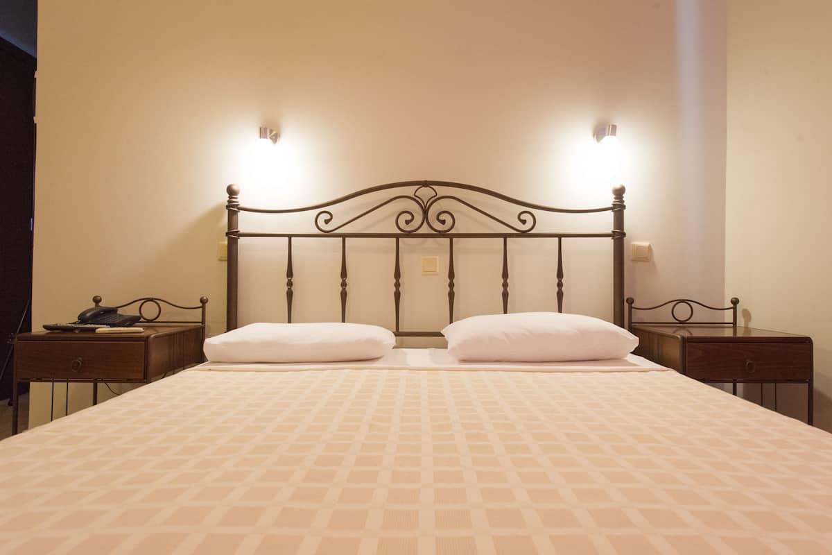 A neatly made bed with a patterned bedspread, two bedside tables with lamps, and a wall-mounted light fixture above the bed.
