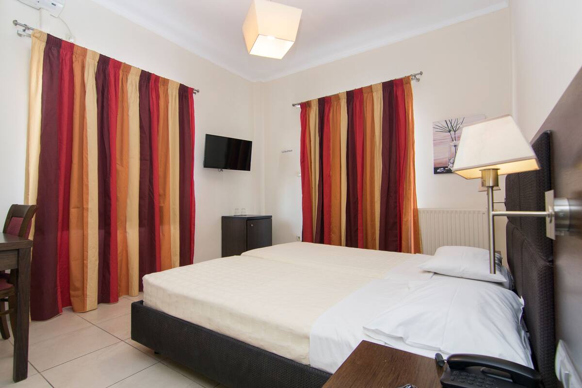 A hotel room with a bed, a desk, a chair, a lamp, a telephone, and curtains.