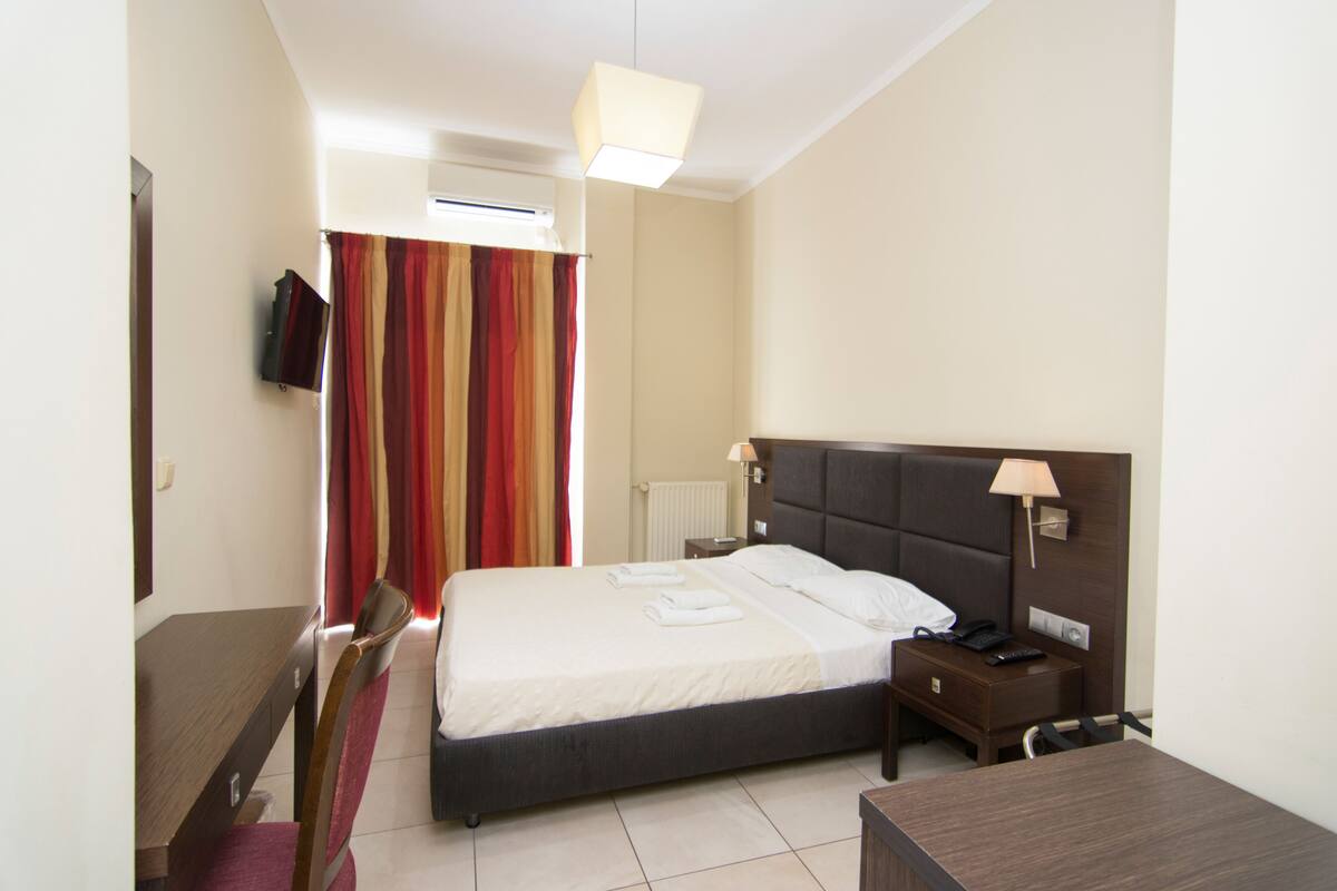 A hotel room with a bed, bedside table, lamp, chair, and a TV mounted on the wall.