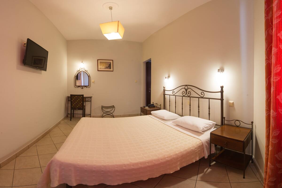 A bedroom with a bed, bedside tables, a nightstand, a chair, a television, and a mirror.