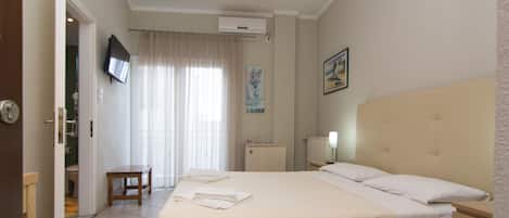 Habitación de hotel con cama, mesita de noche, una silla, televisor y ventana con cortinas.
