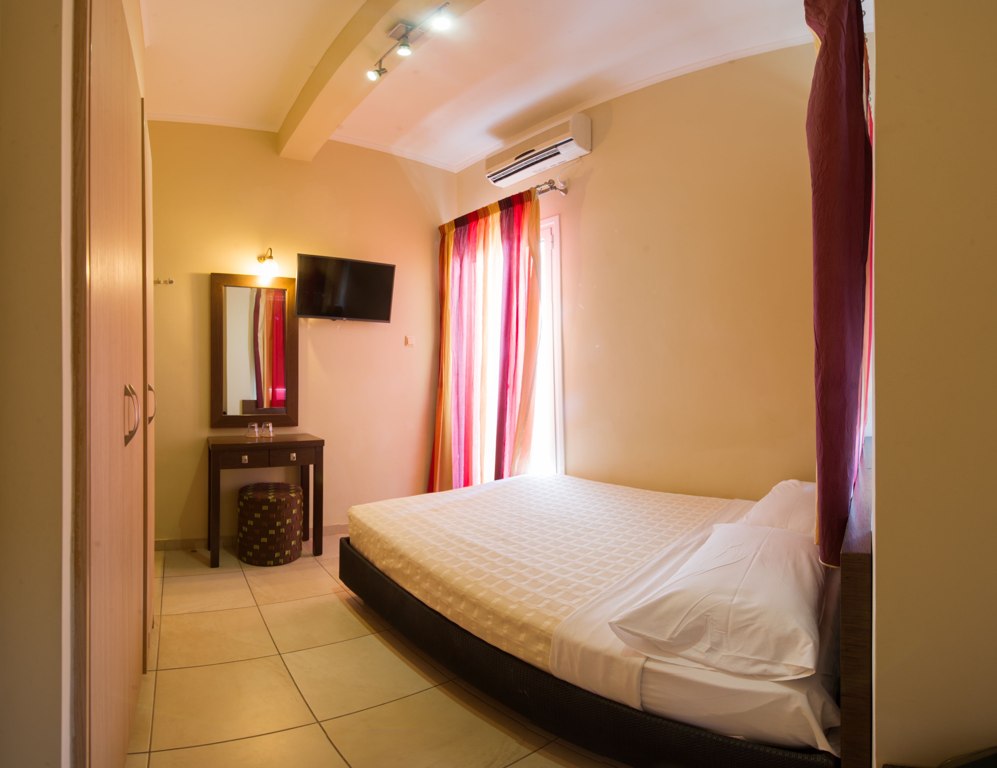 A bedroom with a bed, a television, a mirror, a bedside table, and an air conditioning unit.