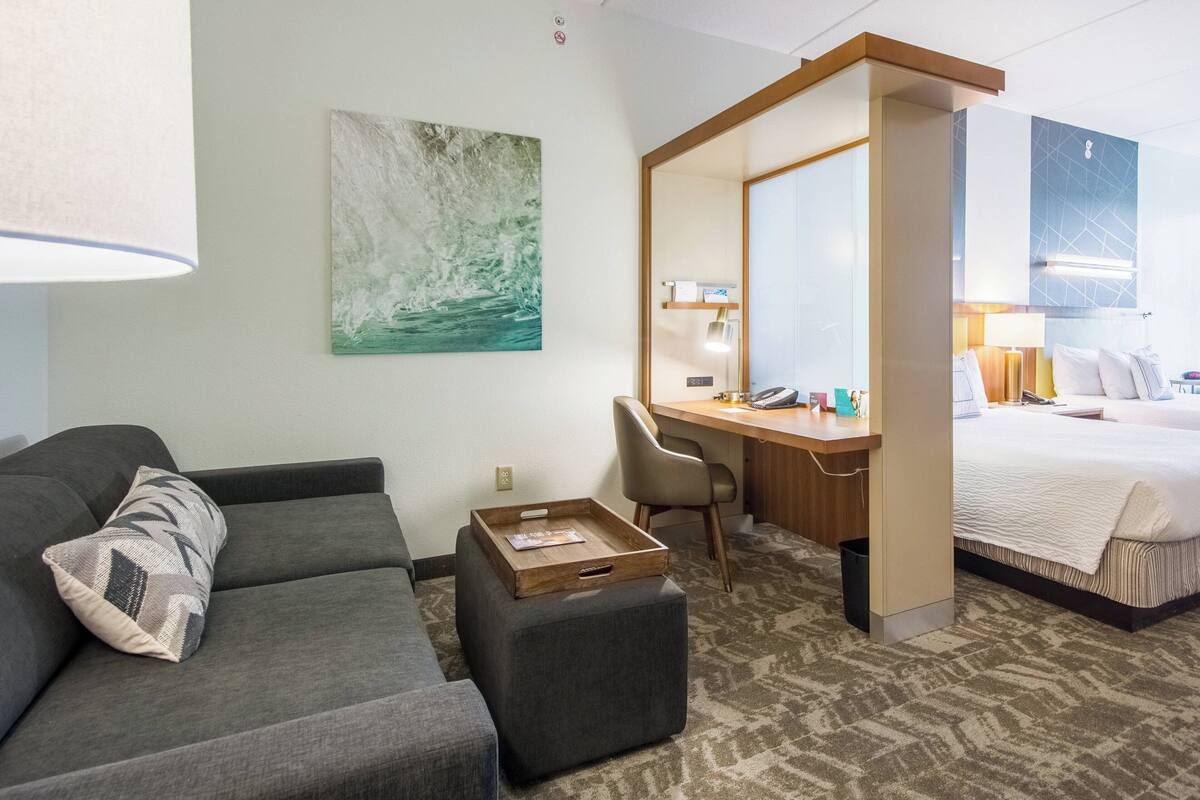 A hotel room with a sofa, a desk, a bed, and a large mirror.