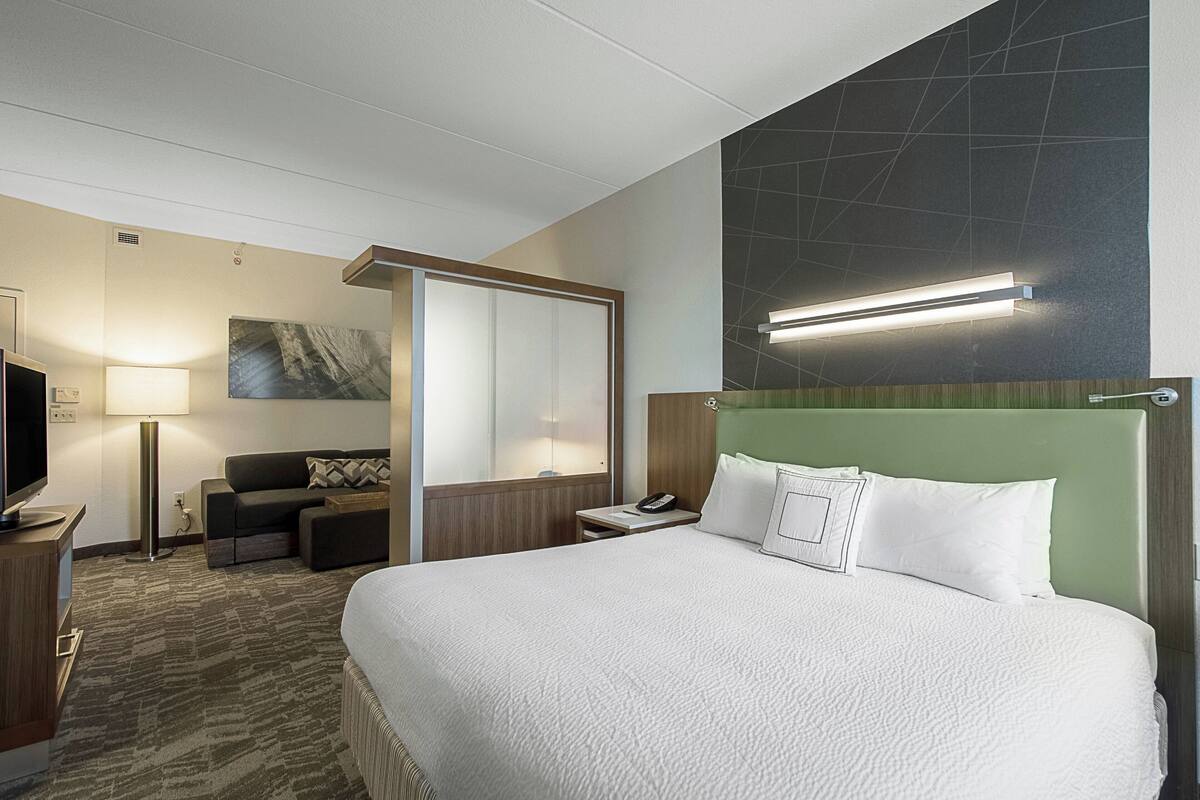 A hotel room with a large bed, a desk with a lamp, a television, and a sofa.