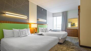 A hotel room with two beds, a large window with curtains, a wooden cabinet, and a wall-mounted light fixture.