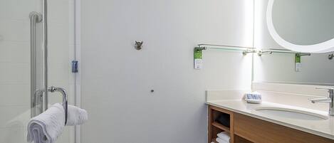Un baño con cabina de ducha de vidrio, tocador de madera con espejo y perchero para toallas.