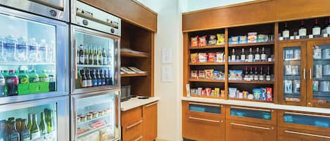 Una cocina con varias neveras repletas de bebidas y alimentos, armarios de madera y una variedad de productos envasados.
