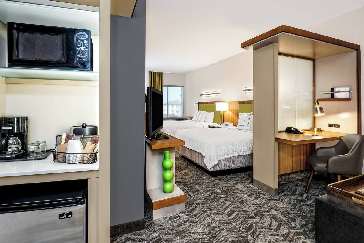 A hotel room with a kitchenette, a bed, a desk, and a TV.