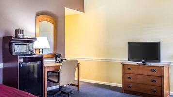 A hotel room with a bed, a desk with a computer, a television, a microwave, and a coffee maker.