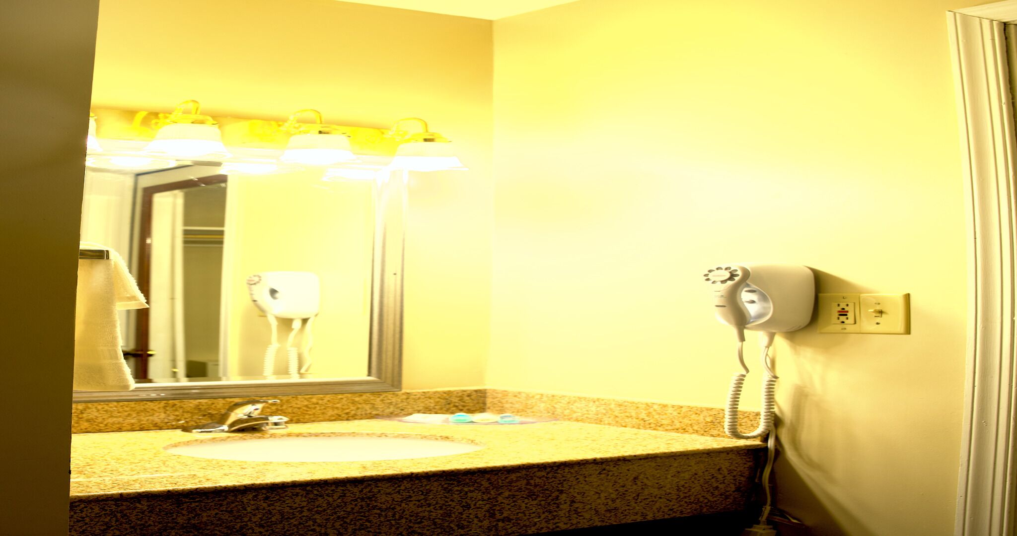 A bathroom with a sink, mirror, hairdryer, and a telephone.