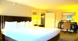 A hotel room with a large bed, a desk, a chair, and a door.