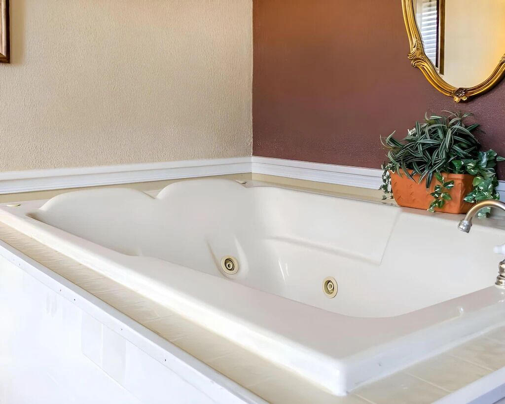 Une grande baignoire blanche avec un seul robinet, placée contre un mur beige, avec un miroir au-dessus.