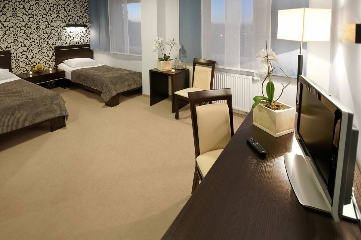 A hotel room with two beds, a desk with a TV, a chair, a small table with a plant, and a window with a view.