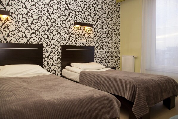 A hotel room with two single beds, a patterned wallpaper, a night light, and a window with curtains. - Hotton Hotel (Gdynia)