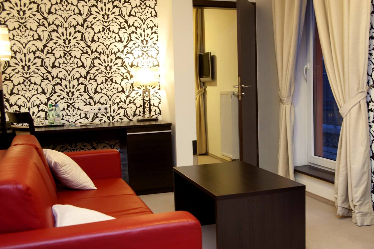 A modern hotel room with a red sofa, a small table, a TV, and a patterned wallpaper.
