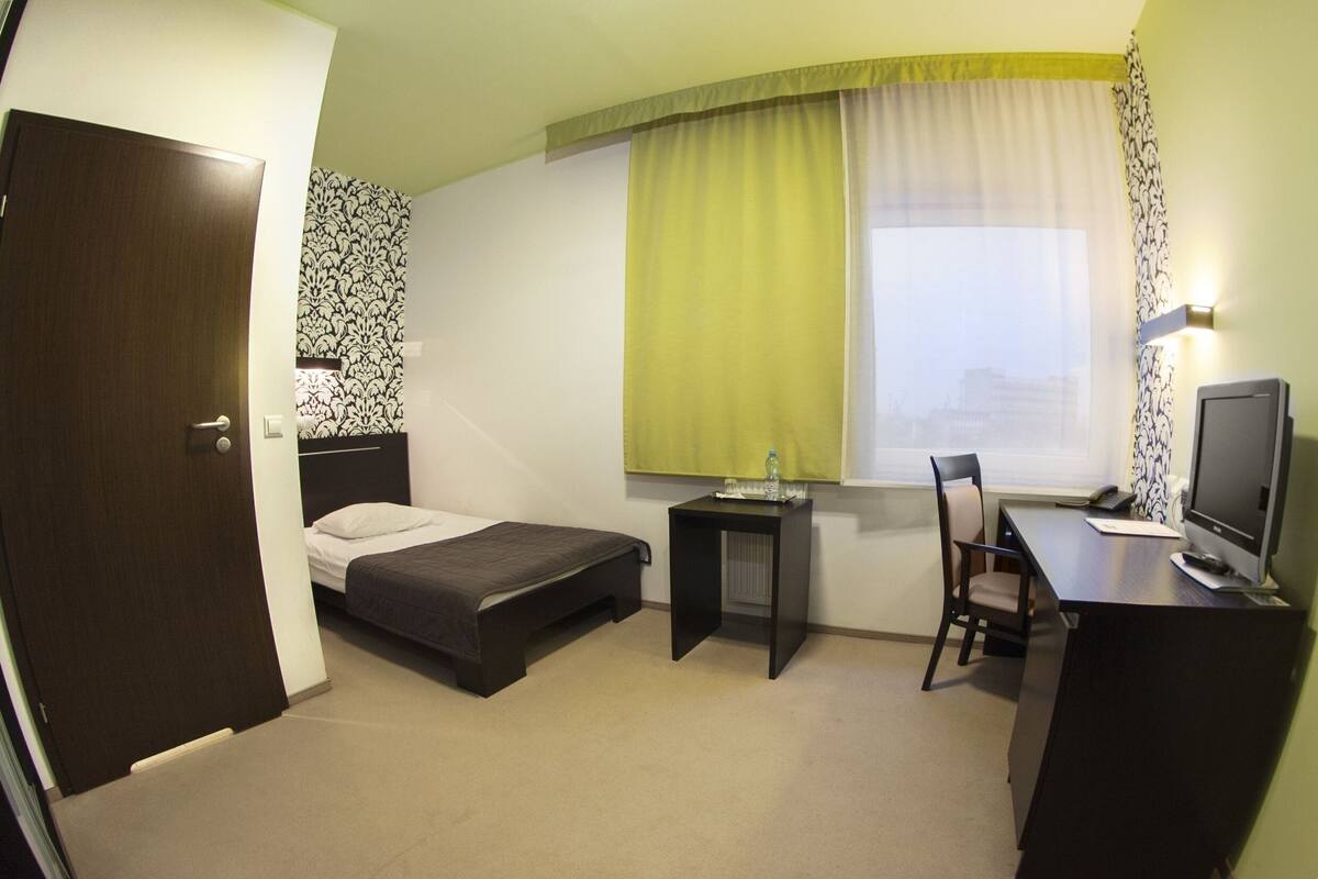 A hotel room with a bed, a desk, a chair, a television, and a window with curtains.