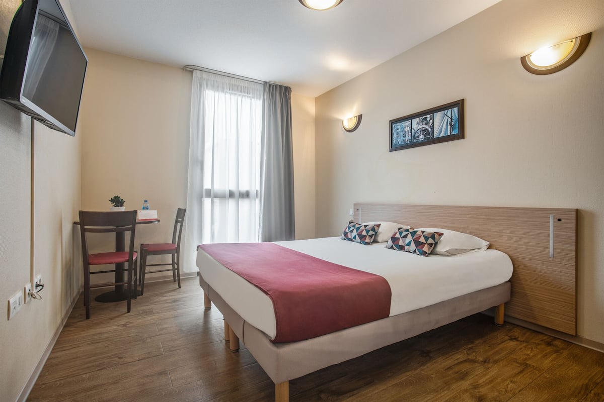A hotel room with a bed, a desk, a chair, a television, and a window with curtains.