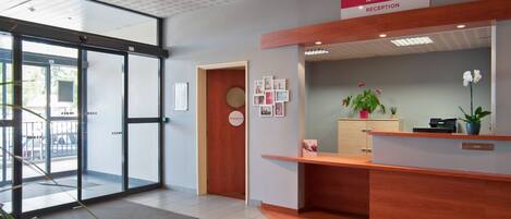A reception area with a wooden reception desk, a reception sign, a door with a circular sign, and a wall with framed pictures.