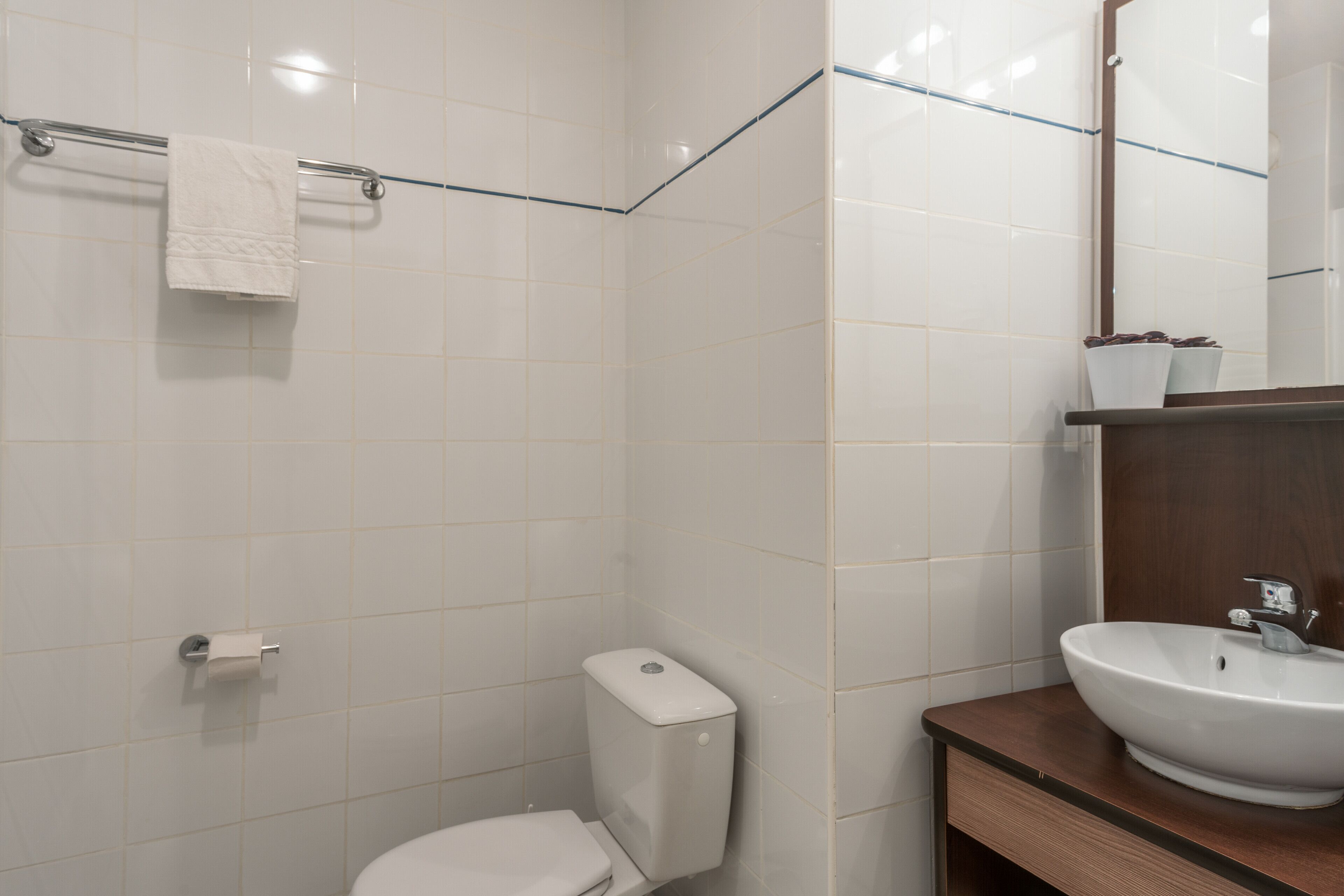 Une salle de bain avec des carreaux blancs, des toilettes, un lavabo et un porte-serviettes.
