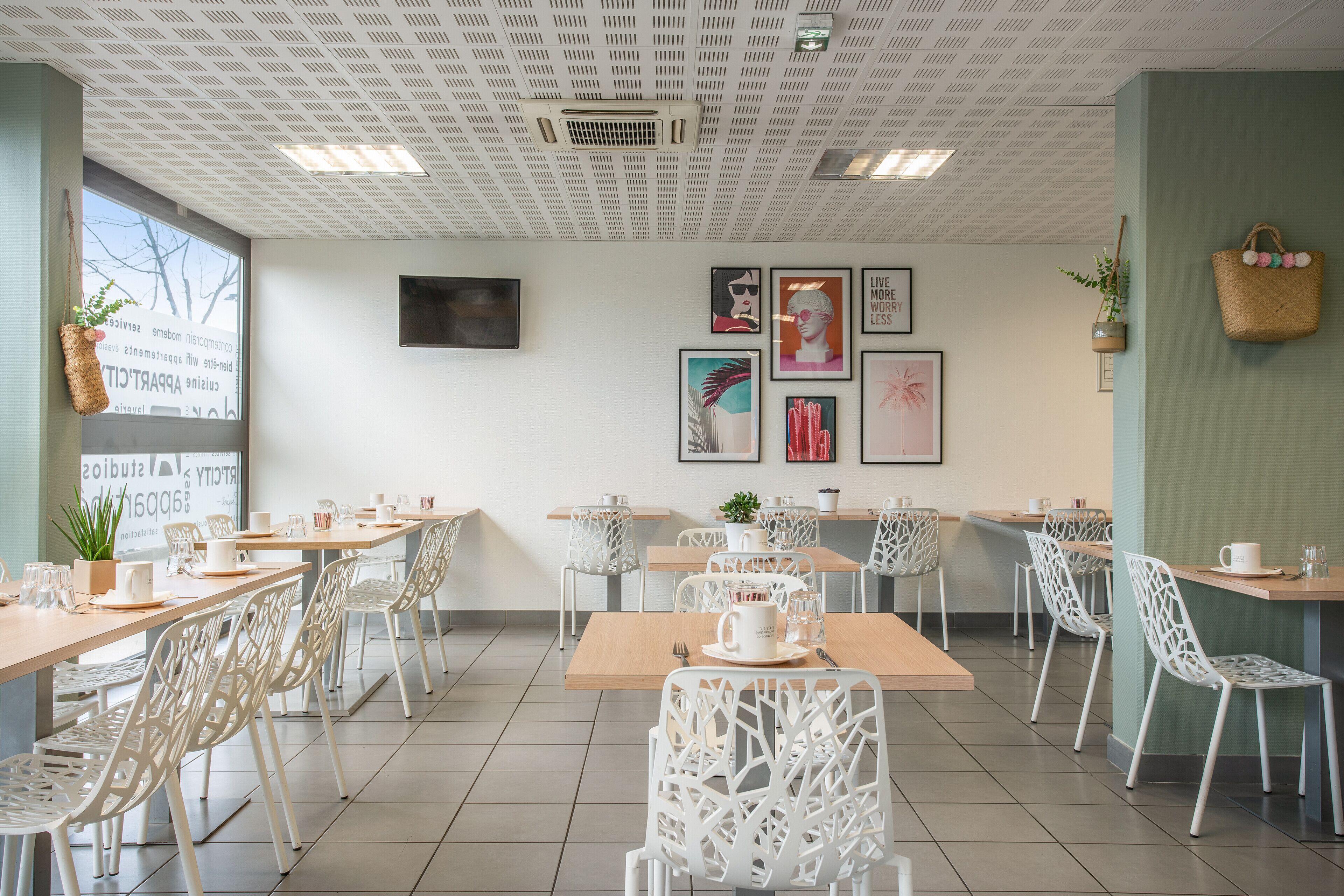 Un café moderno con sillas blancas, mesas de madera y un techo con un diseño geométrico.
