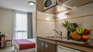 A compact hotel room with a bed, a small kitchenette, a dining area, and a bathroom. - Appart'City Classic Nîmes Centre (Nîmes)