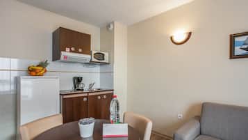 Cocina compacta con microondas, cafetera y frutero en la encimera.