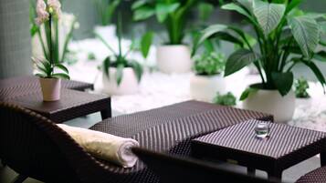Un patio con mobiliario de mimbre, plantas en macetas y un vaso sobre una de las mesas.