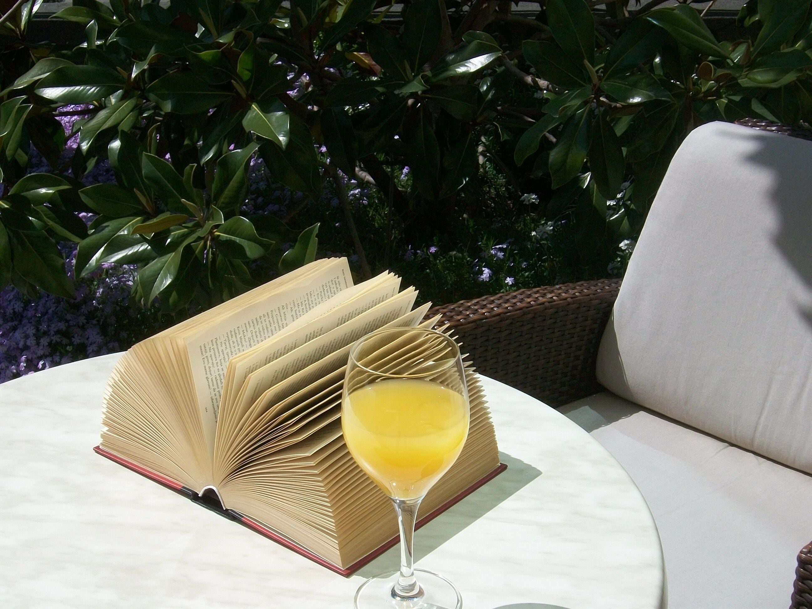 Un libro abierto sobre una mesa, un vaso de jugo de naranja y una silla de mimbre.