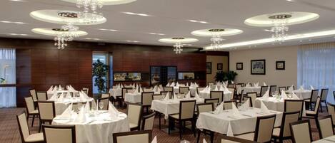 A banquet hall with round tables set for dining, featuring a modern chandelier design and a warm, inviting atmosphere.