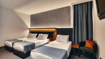 Habitación de hotel con dos camas individuales, un sillón pequeño, televisión y un ventanal con cortinas.