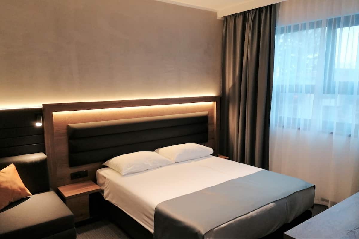 A hotel room with a large bed, a nightstand, a seating area, and a window with curtains.