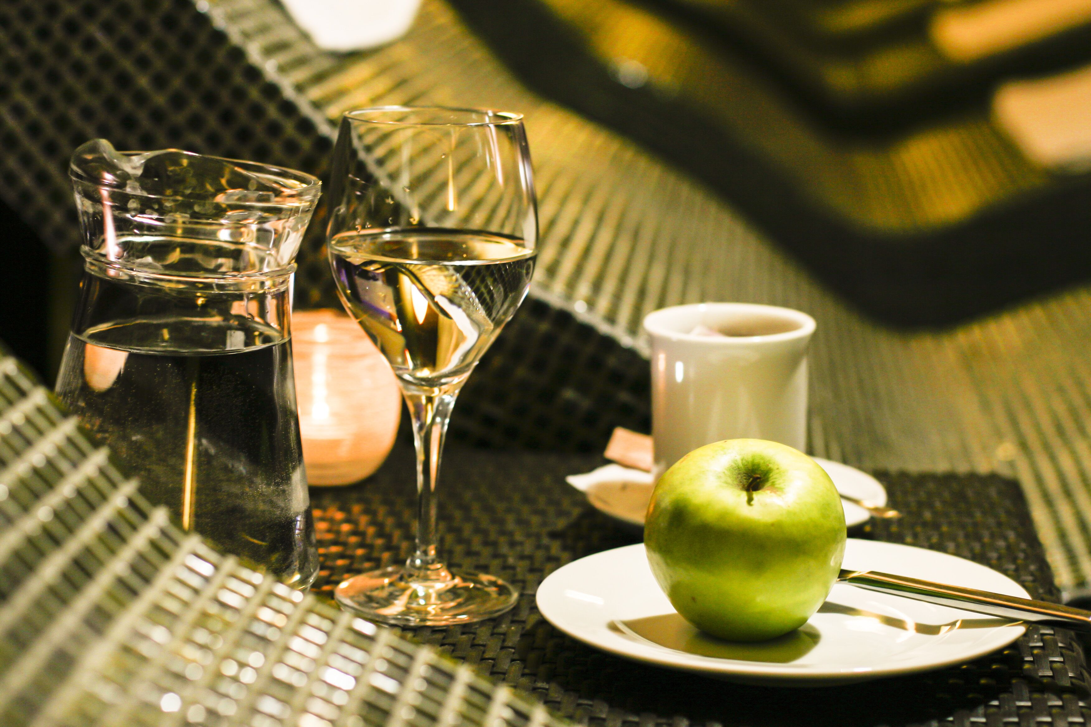 Una mesa con una manzana verde, un vaso de agua, una copa de vino y una taza.