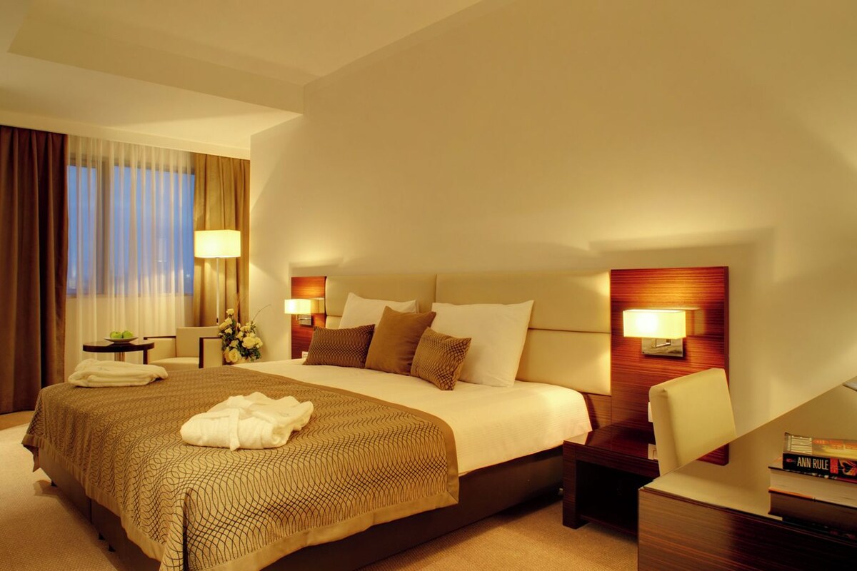 A hotel room with a large bed, bedside tables, a desk, and a chair.
