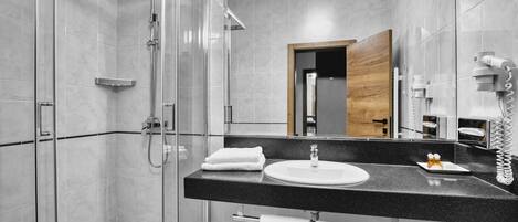Un baño moderno con ducha envuelta en vidrio, lavamanos de superficie negra y un espejo grande.