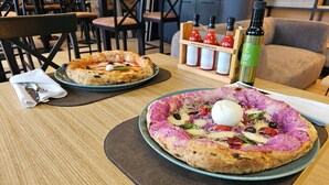Two pizzas on plates, a bottle of olive oil, and a bottle of hot sauce on a table. - Hotel Aristos (Zagreb)