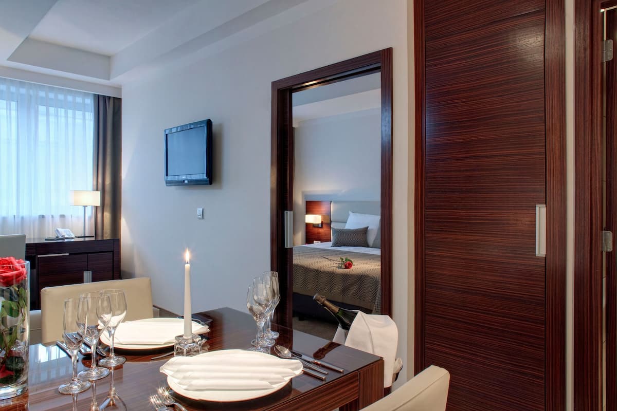A hotel room with a dining table set for four, a TV mounted on the wall, and a large mirror reflecting the room.