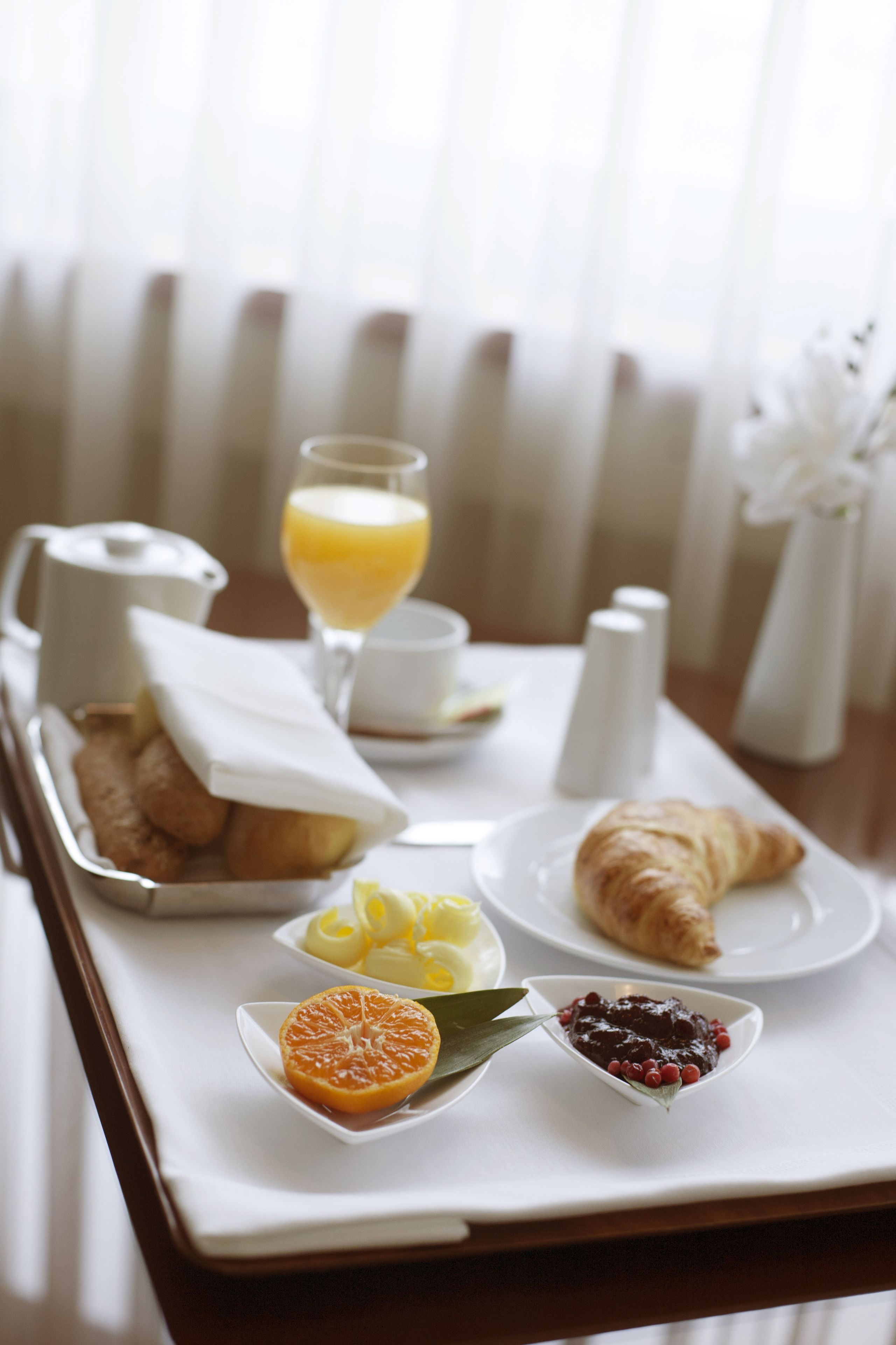 Un plateau de petit-déjeuner avec des croissants, des tranches d’orange et de la confiture, posé sur une table blanche.