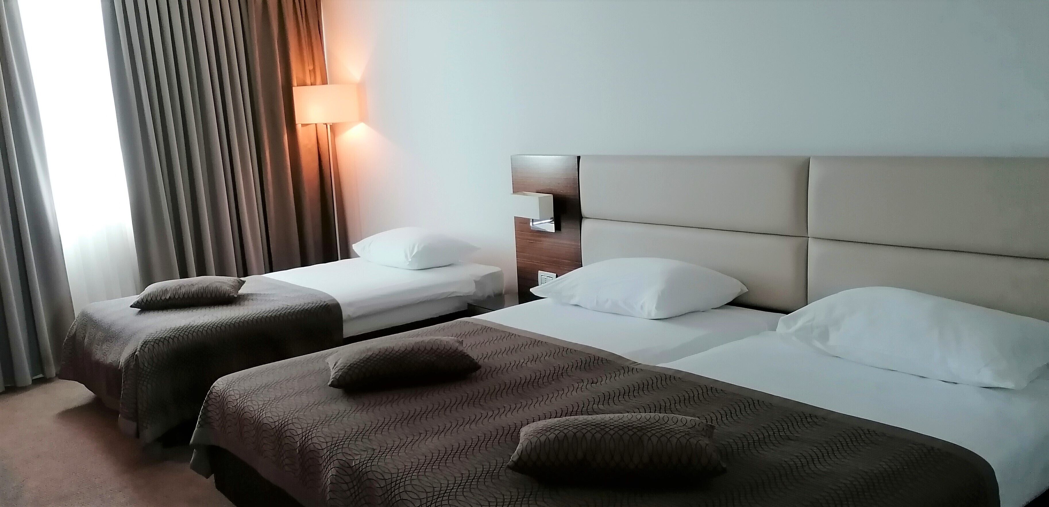 A hotel room with two beds, each with a headboard and a bedside lamp.