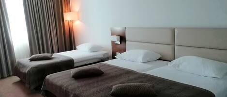 A hotel room with two beds, each with a headboard and a bedside lamp.