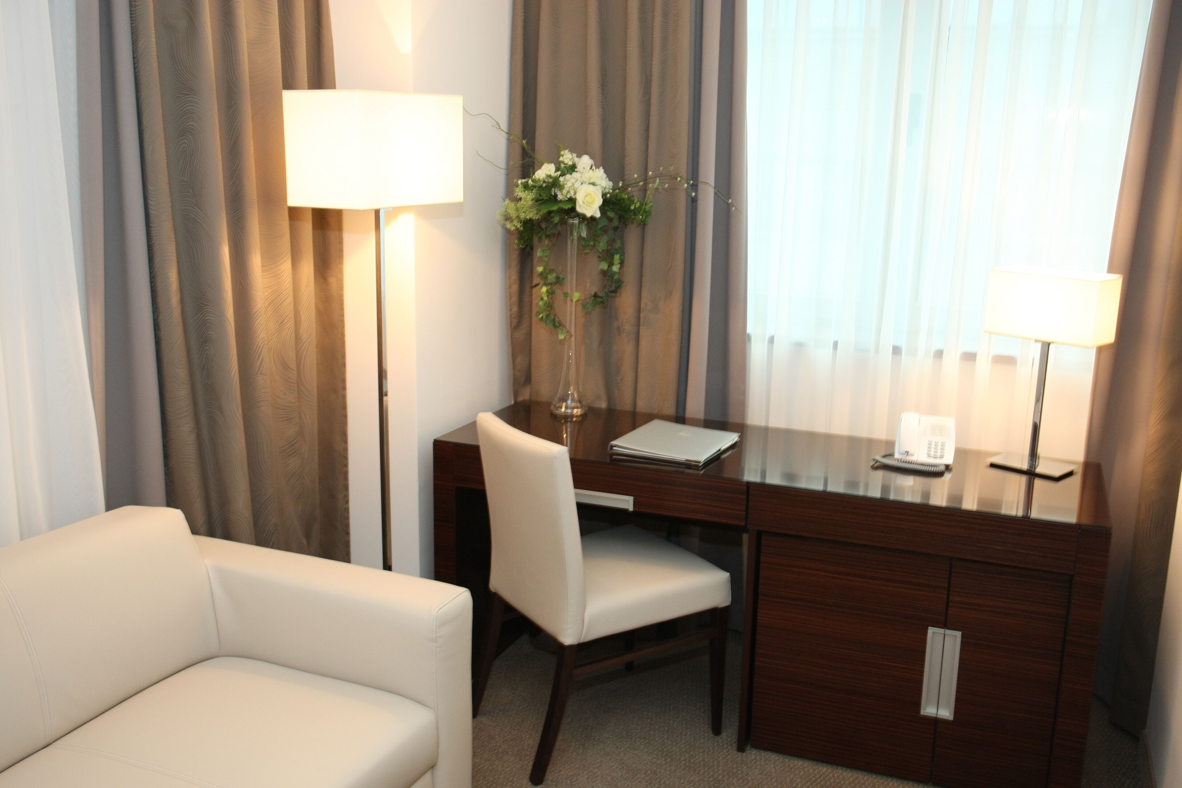 Une chambre d’hôtel équipée d’un bureau, d’une chaise, d’une lampe et d’un vase avec des fleurs.