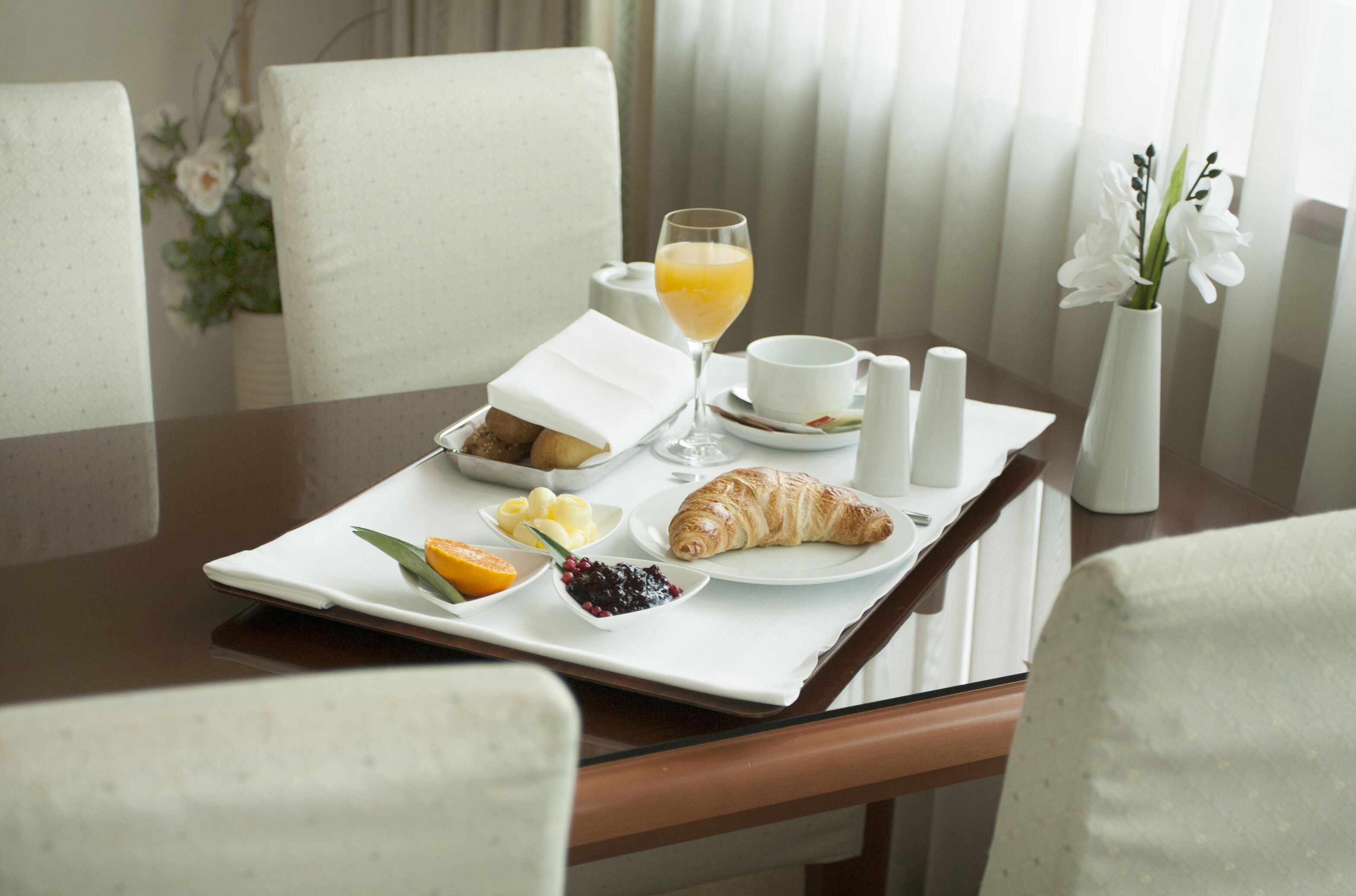 Un plateau de petit-déjeuner avec des croissants, des fruits et du jus, posé sur une table dans une chambre d’hôtel.