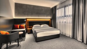 A modern hotel room with a bed, a sofa, a small table, and a large window with curtains. - Hotel Aristos (Zagreb)