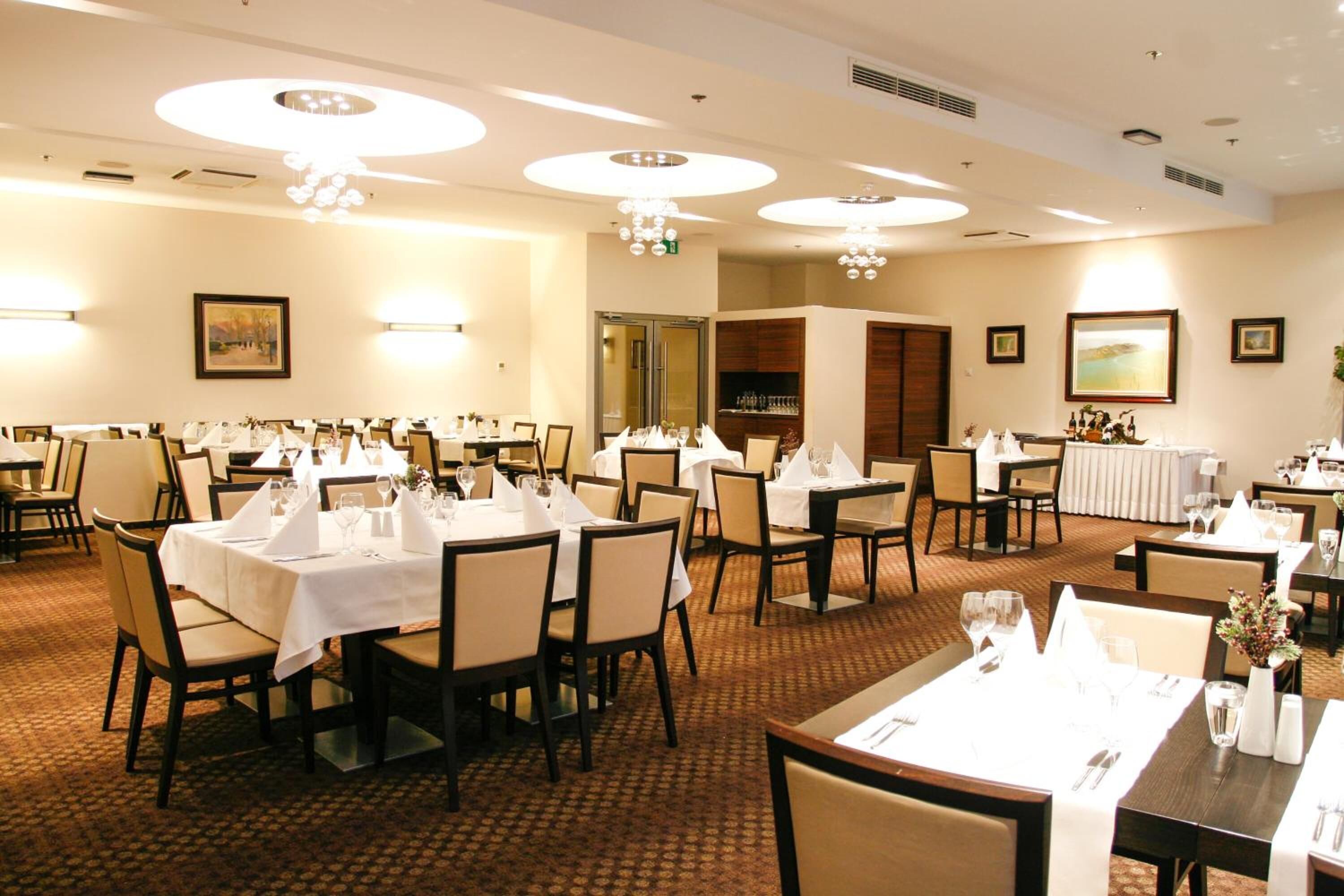 A hotel dining area with round tables, chairs, and chandeliers.
